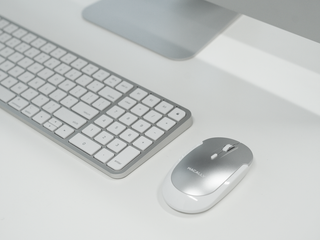 Sleek white keyboard and silver Macally mouse on a clean minimalist desk beneath a modern computer stand